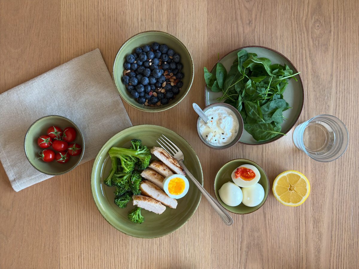 An overhead flat lay of oats, berries, eggs, chicken, vegetables and water